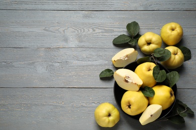 Photo of Fresh ripe organic quinces with leaves on grey wooden table, flat lay. Space for text