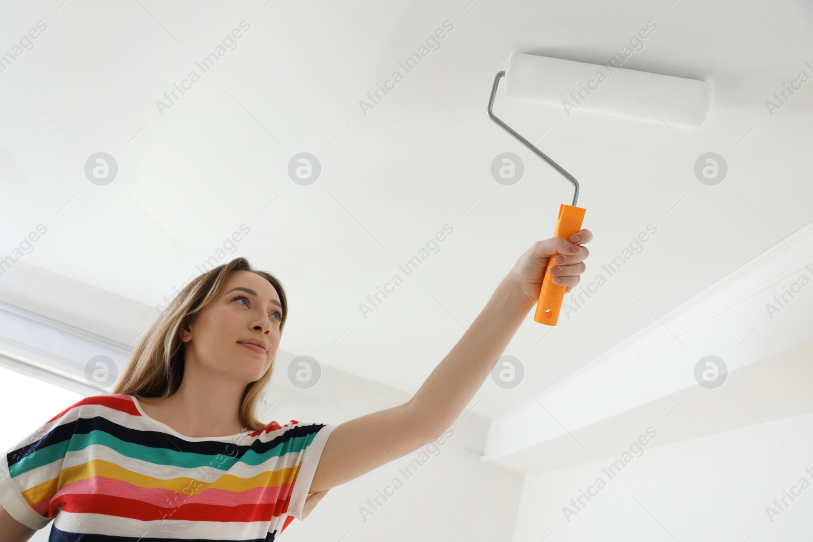 Photo of Young woman painting ceiling with white dye indoors