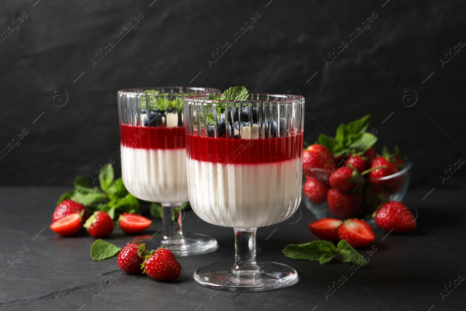 Delicious panna cotta with fruit coulis and fresh berries on dark grey table Photo of Delicious panna cotta with fruit coulis and fresh berries on dark grey table