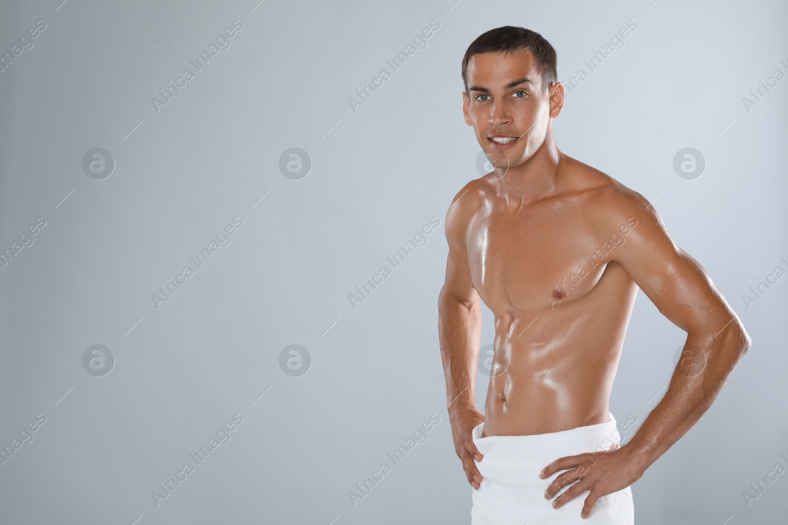 Handsome shirtless man with slim body and towel wrapped around his hips on grey background. Space for text Photo of Handsome shirtless man with slim body and towel wrapped around his hips on grey background. Space for text