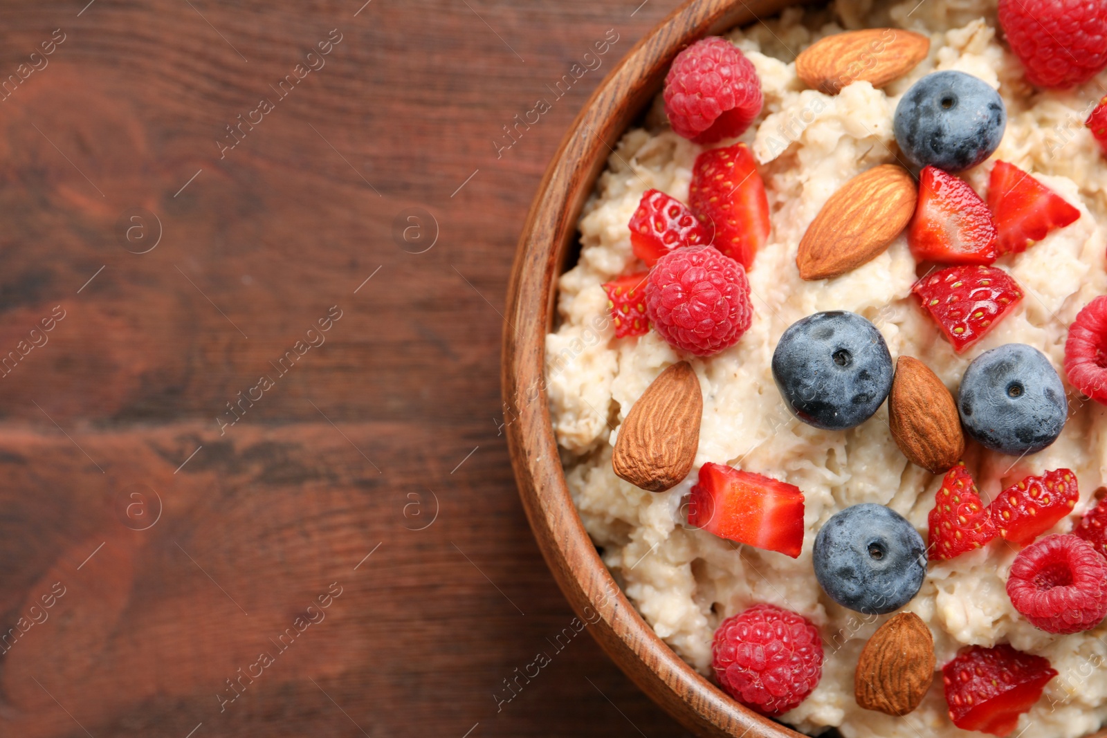 Tasty oatmeal porridge with berries and almond nuts in bowl on wooden table, top view. Space for text Photo of Tasty oatmeal porridge with berries and almond nuts in bowl on wooden table, top view. Space for text