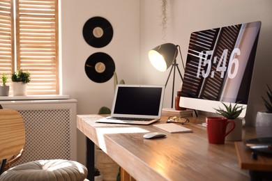 Modern computer and laptop on wooden desk in room. Interior design Photo of Modern computer and laptop on wooden desk in room. Interior design