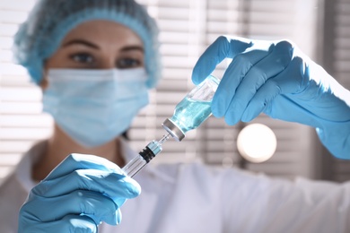 Woman filling syringe with vaccine from vial against blurred background, focus on hands Photo of Woman filling syringe with vaccine from vial against blurred background, focus on hands