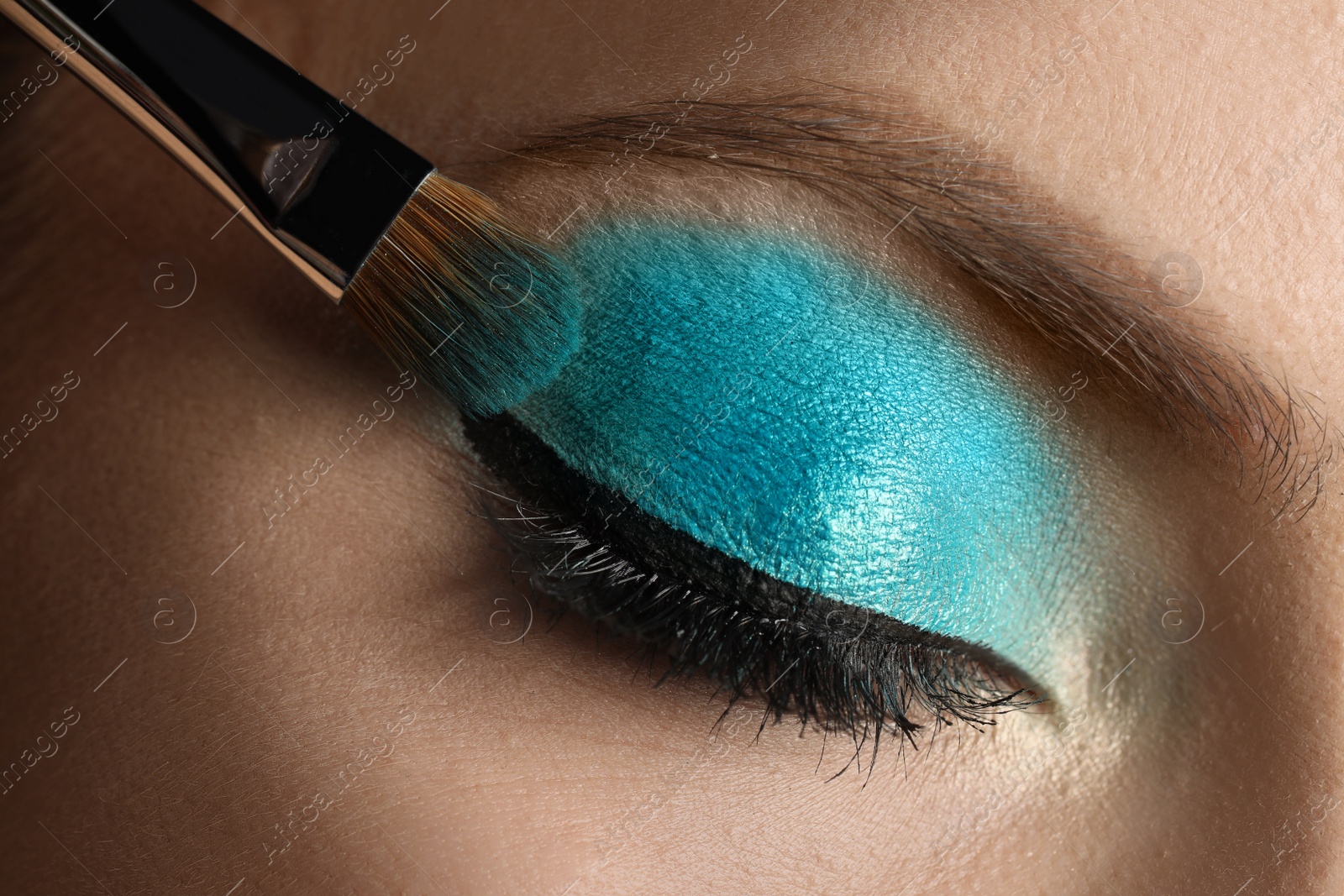Applying cyan eye shadow onto woman's face, closeup. Beautiful evening makeup Photo of Applying cyan eye shadow onto woman's face, closeup. Beautiful evening makeup