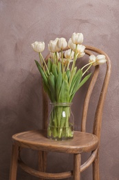 Vase with beautiful tulips on chair, indoors Photo of Vase with beautiful tulips on chair, indoors