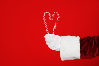 Santa Claus holding candy canes on red background, closeup of hand Photo of Santa Claus holding candy canes on red background, closeup of hand