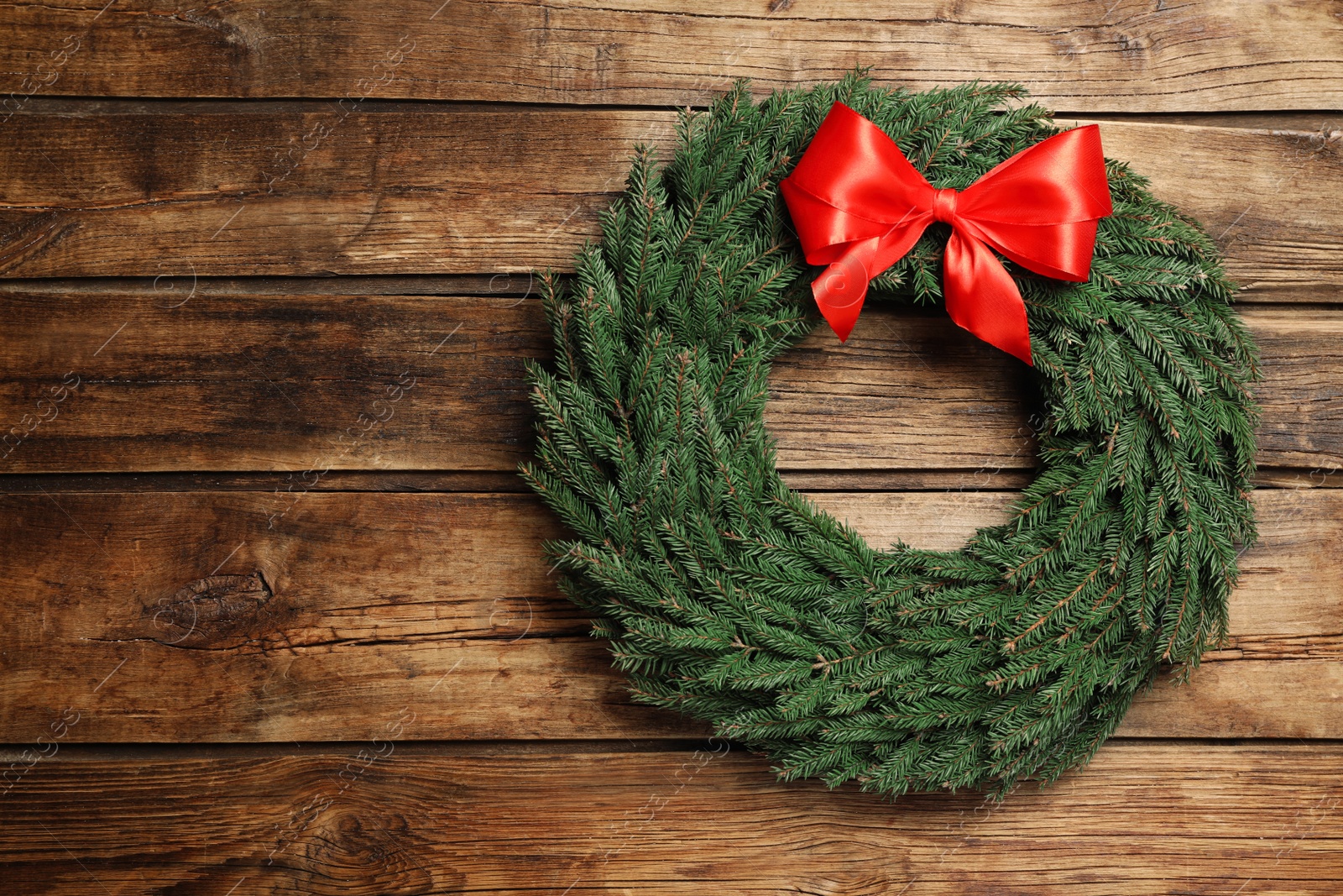 Christmas wreath made of fir branches with red bow on wooden background, top view. Space for text Photo of Christmas wreath made of fir branches with red bow on wooden background, top view. Space for text
