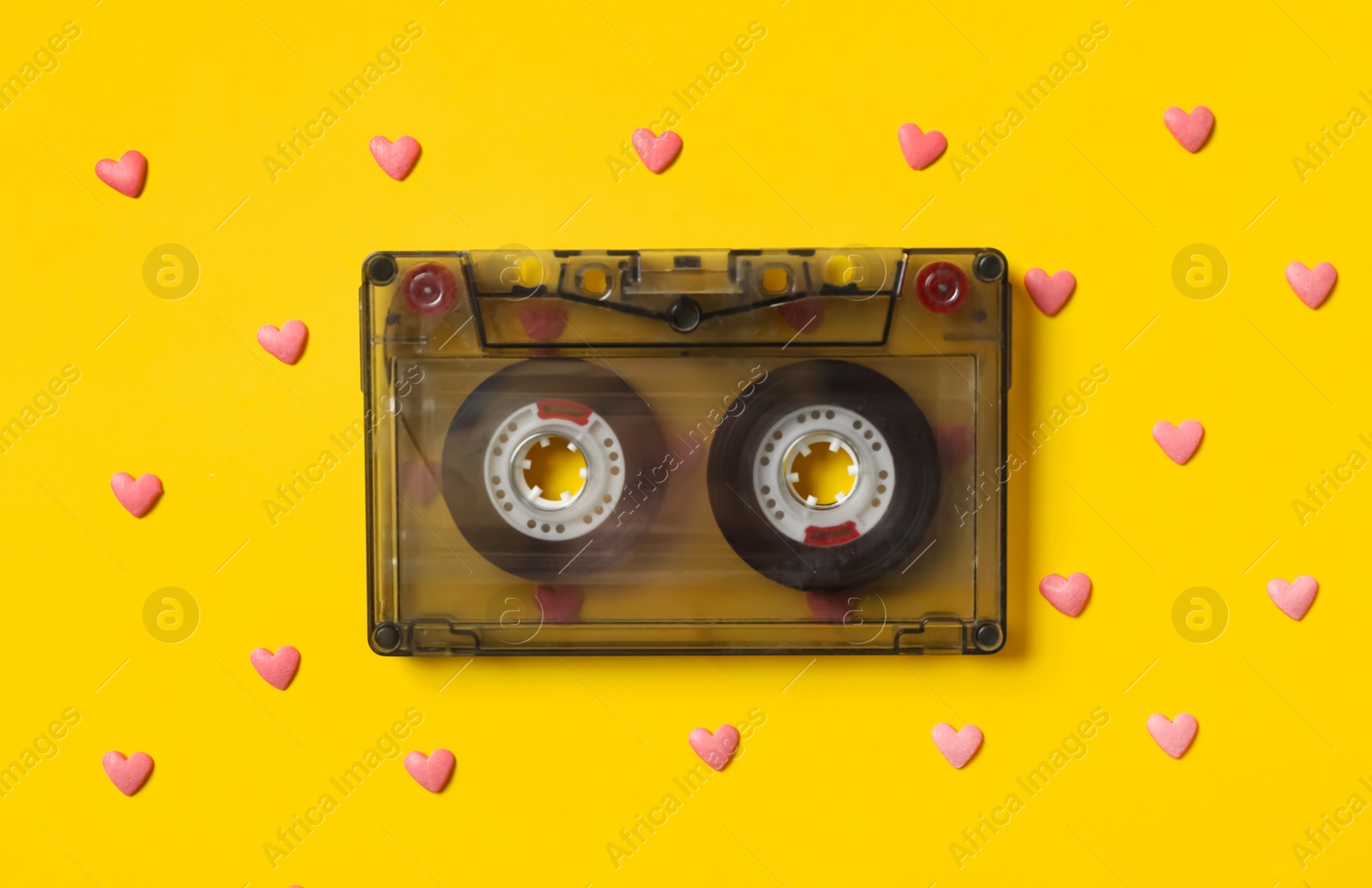 Music cassette and pink heart shaped sprinkles on yellow background, flat lay. Listening love songs Photo of Music cassette and pink heart shaped sprinkles on yellow background, flat lay. Listening love songs