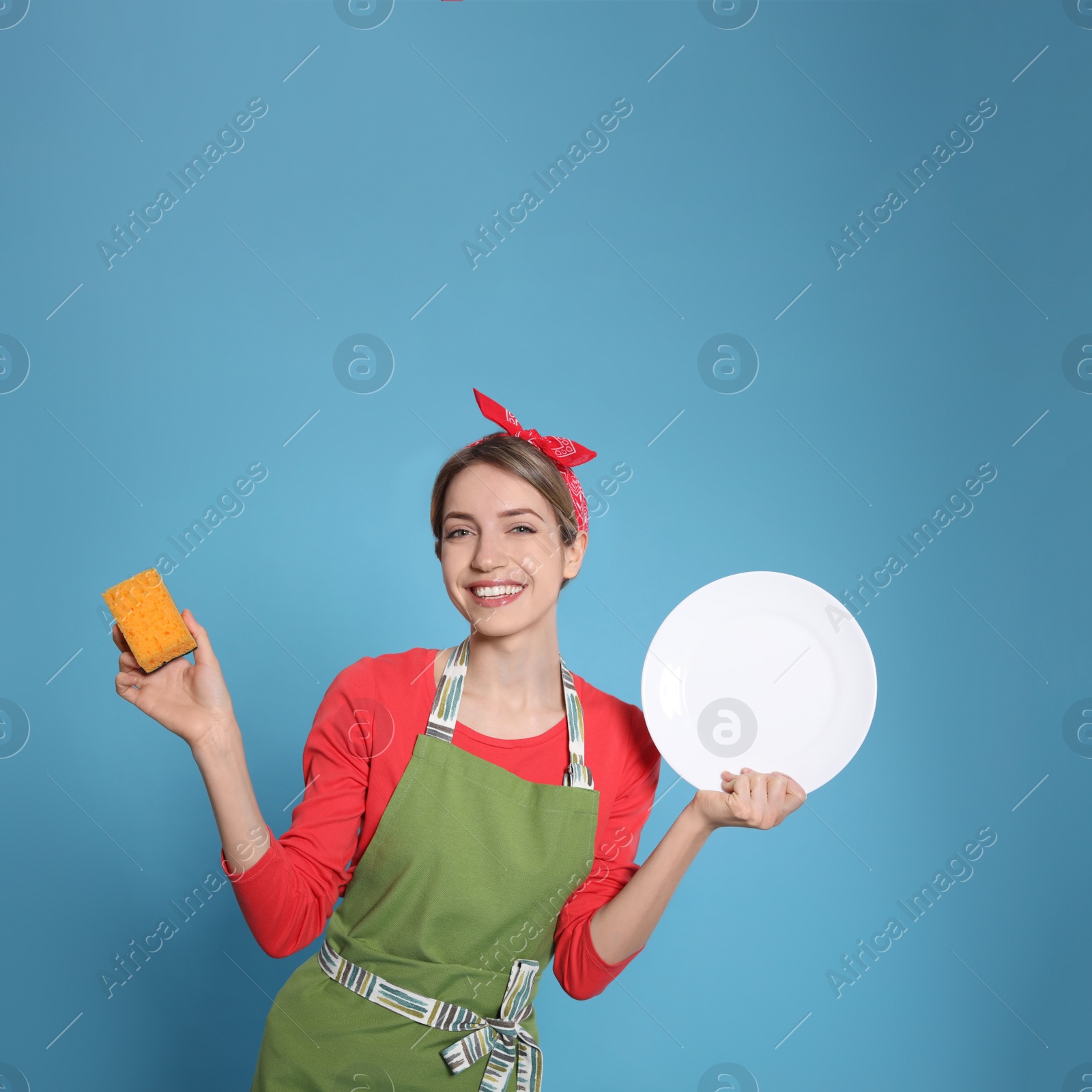 Young housewife with plate and sponge on light blue background Photo of Young housewife with plate and sponge on light blue background