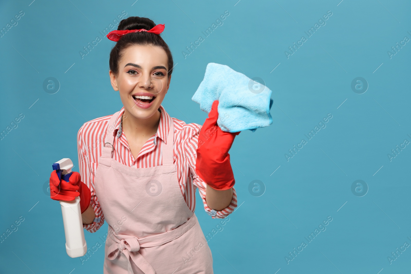 Young housewife with detergent and rug on light blue background, space for text Photo of Young housewife with detergent and rug on light blue background, space for text