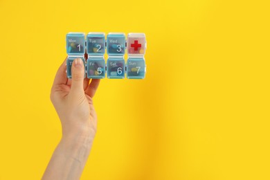 Woman holding plastic box with different pills on yellow background, closeup. Space for text Photo of Woman holding plastic box with different pills on yellow background, closeup. Space for text