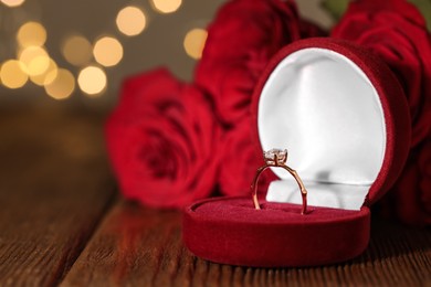 Beautiful engagement ring with gemstone in box and roses on wooden table Photo of Beautiful engagement ring with gemstone in box and roses on wooden table