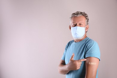 Senior man in protective mask pointing at arm with bandage after vaccination on beige background. Space for text Photo of Senior man in protective mask pointing at arm with bandage after vaccination on beige background. Space for text
