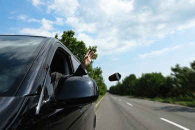 Driver throwing away paper coffee cup from car window. Garbage on road Photo of Driver throwing away paper coffee cup from car window. Garbage on road