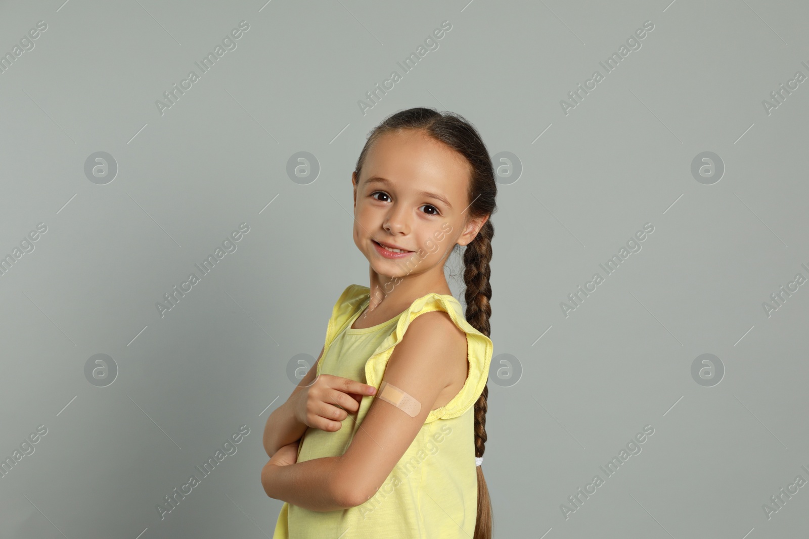Vaccinated little girl showing medical plaster on her arm against light grey background Photo of Vaccinated little girl showing medical plaster on her arm against light grey background