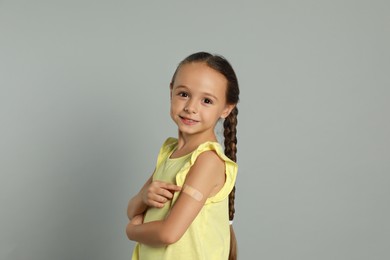 Vaccinated little girl showing medical plaster on her arm against light grey background Photo of Vaccinated little girl showing medical plaster on her arm against light grey background