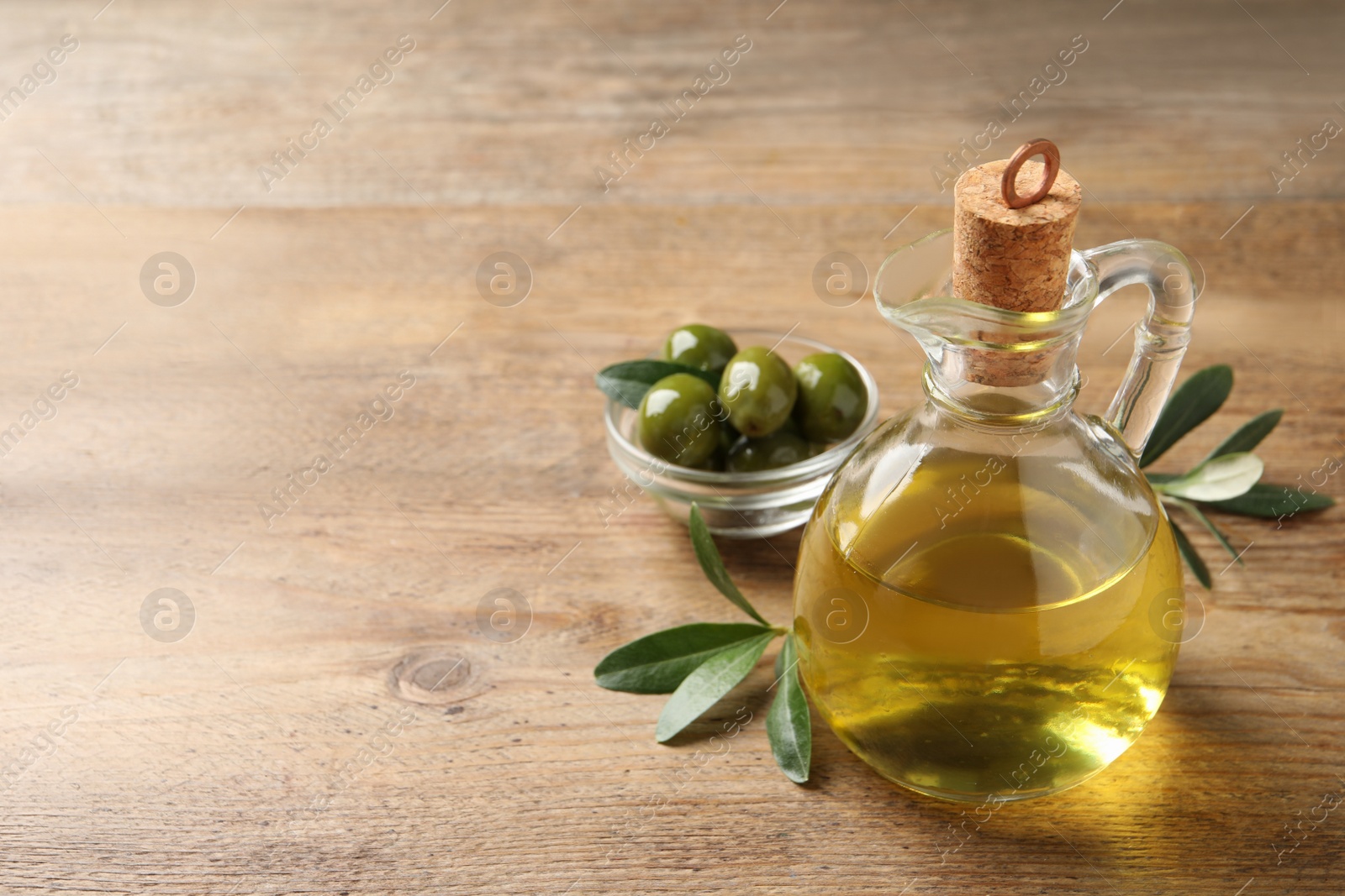 Glass jug of oil, ripe olives and green leaves on wooden table. Space for text Photo of Glass jug of oil, ripe olives and green leaves on wooden table. Space for text