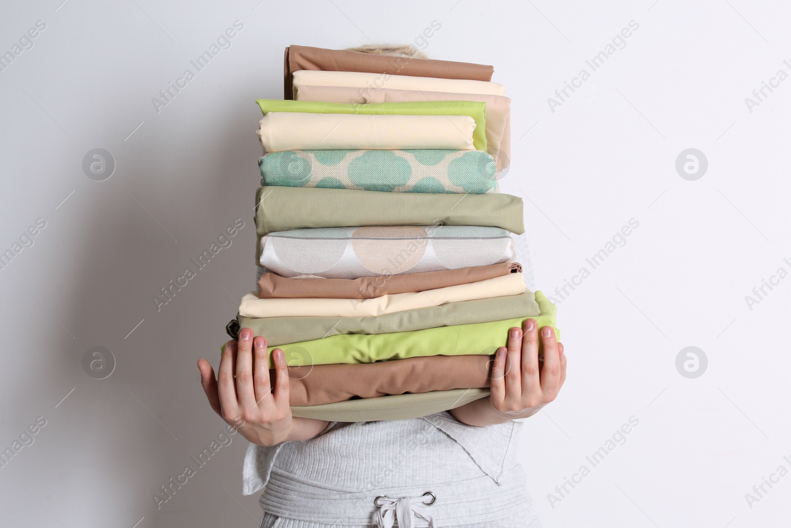 Woman holding stack of clean bed linens on white background Photo of Woman holding stack of clean bed linens on white background