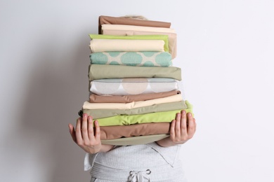 Woman holding stack of clean bed linens on white background Photo of Woman holding stack of clean bed linens on white background