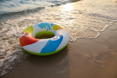 Bright inflatable ring on sunlit sandy beach near sea, space for text Photo of Bright inflatable ring on sunlit sandy beach near sea, space for text