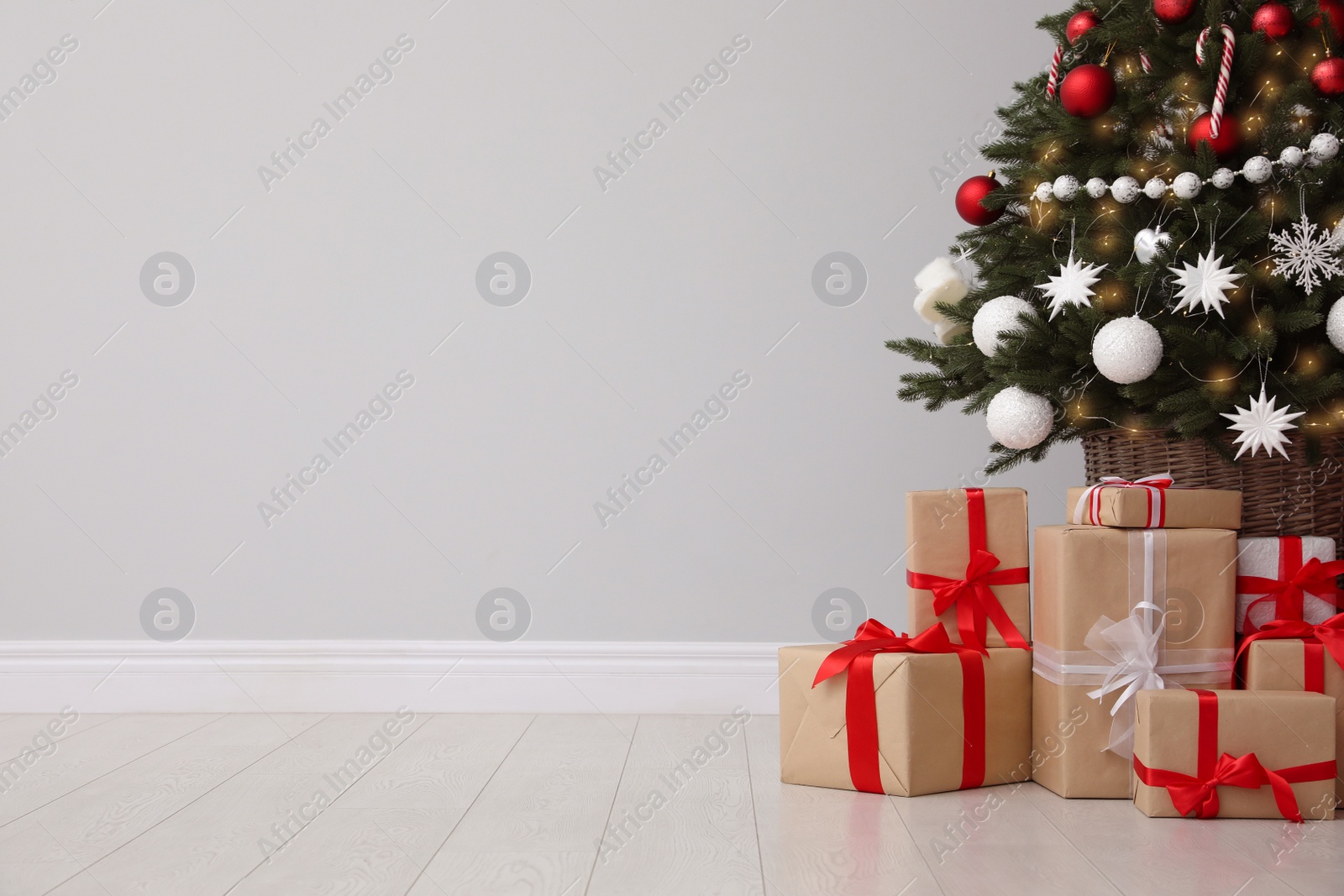 Gift boxes under decorated Christmas tree near grey wall. Space for text Photo of Gift boxes under decorated Christmas tree near grey wall. Space for text