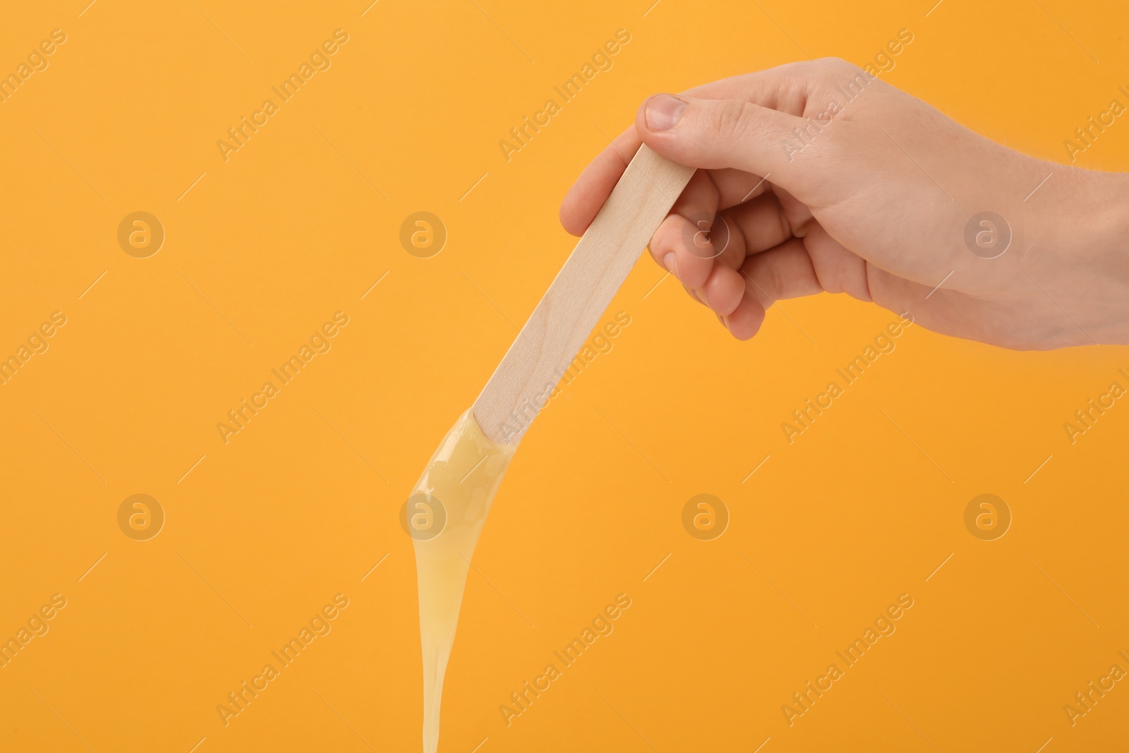 Woman holding spatula with hot depilatory wax on yellow background, closeup Photo of Woman holding spatula with hot depilatory wax on yellow background, closeup