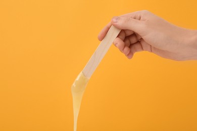 Woman holding spatula with hot depilatory wax on yellow background, closeup Photo of Woman holding spatula with hot depilatory wax on yellow background, closeup