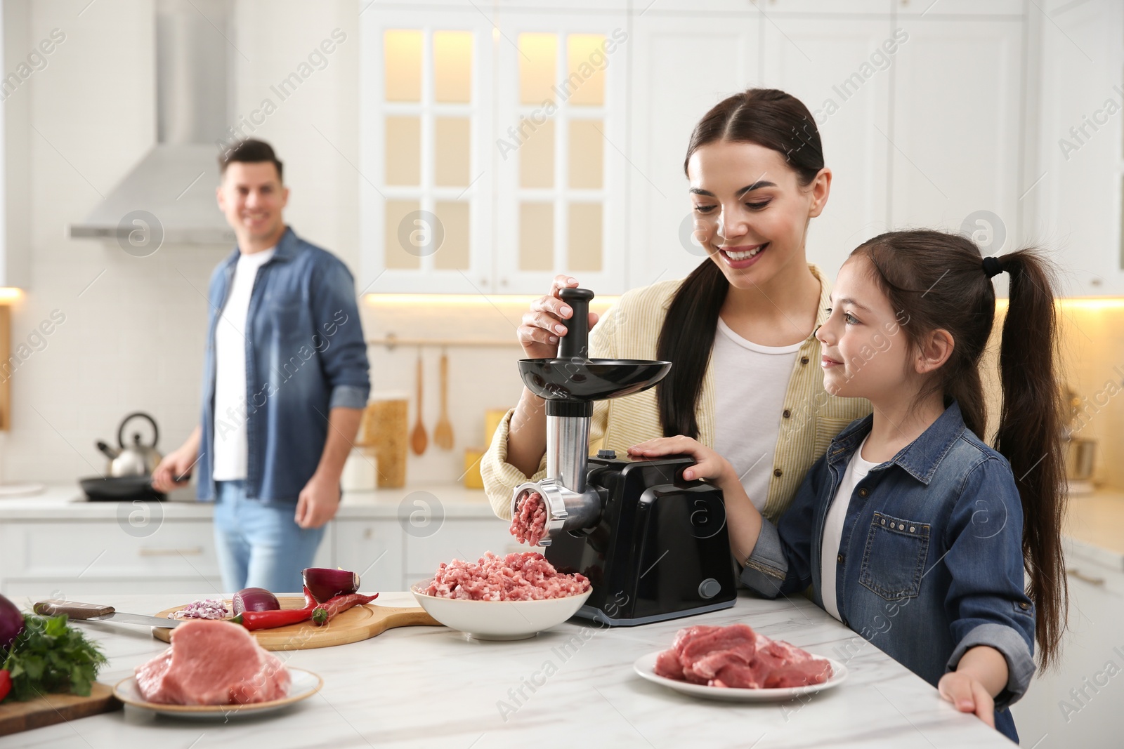 Happy family making dinner together in kitchen, mother and daughter using modern meat grinder Photo of Happy family making dinner together in kitchen, mother and daughter using modern meat grinder