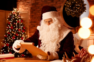 Santa Claus reading wish list at table indoors Photo of Santa Claus reading wish list at table indoors