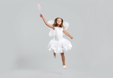 Cute little girl in fairy costume with wings and magic wand on light background Photo of Cute little girl in fairy costume with wings and magic wand on light background