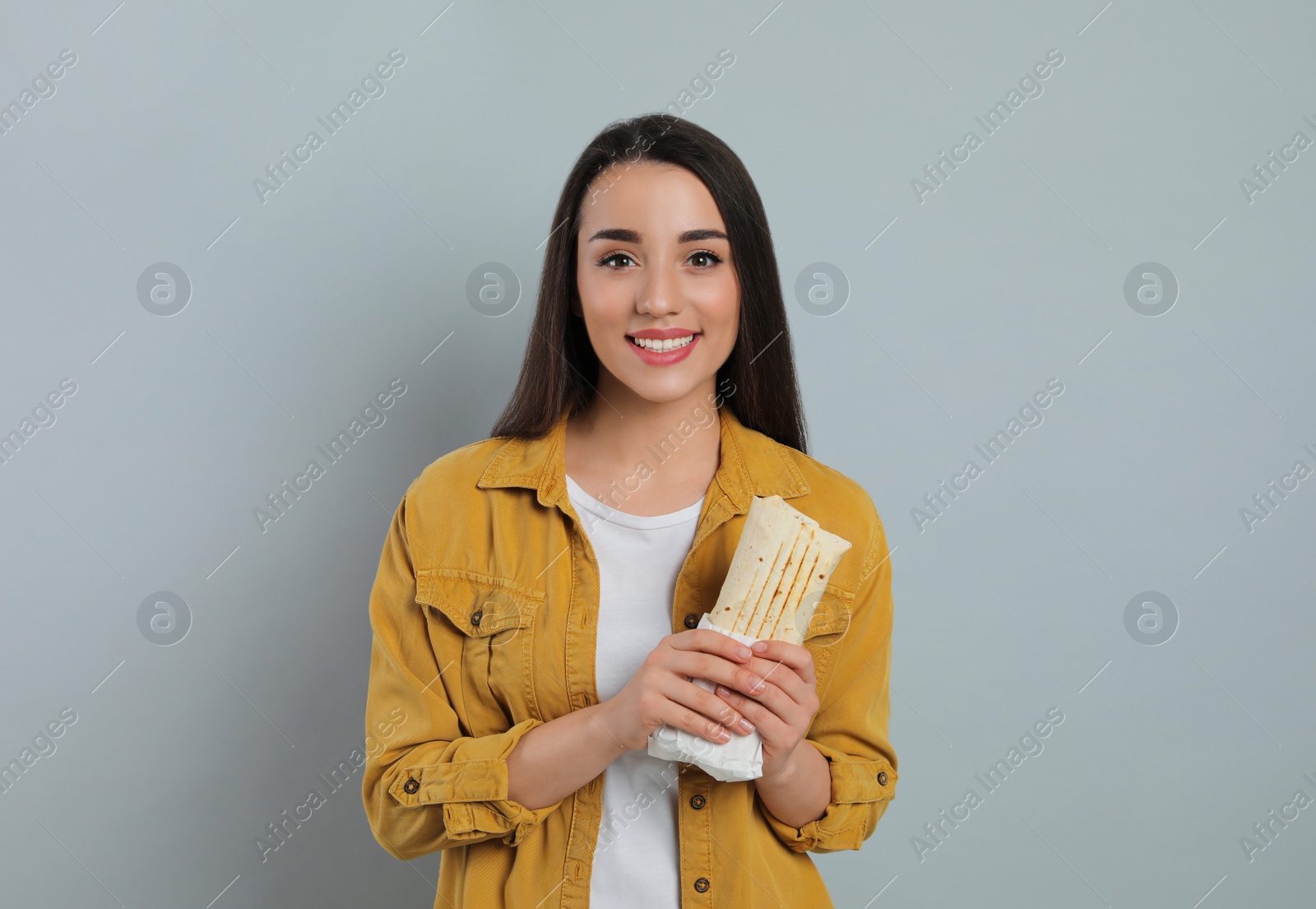 Happy young woman holding tasty shawarma on grey background Photo of Happy young woman holding tasty shawarma on grey background