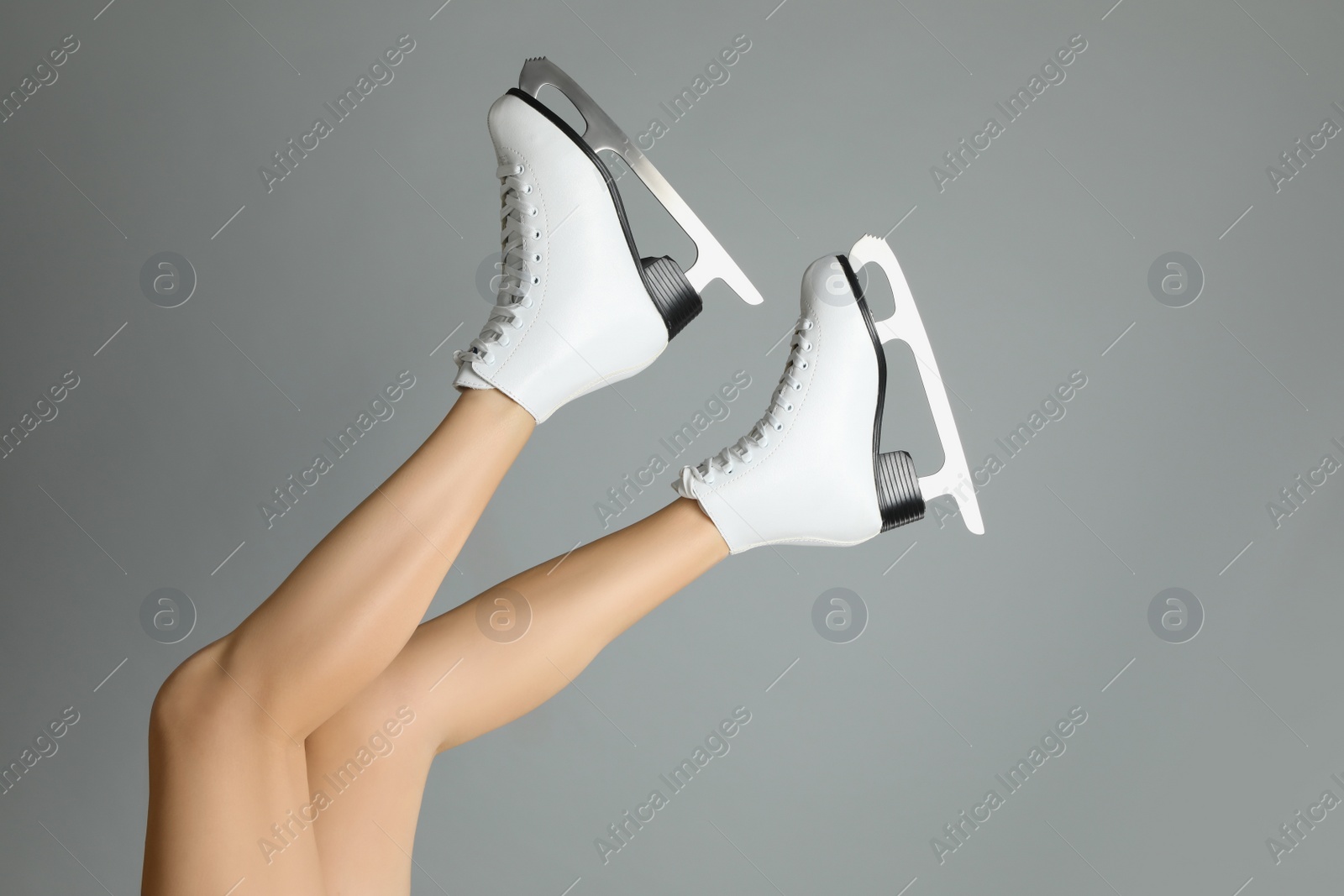 Woman in elegant white ice skates on grey background, closeup of legs Photo of Woman in elegant white ice skates on grey background, closeup of legs