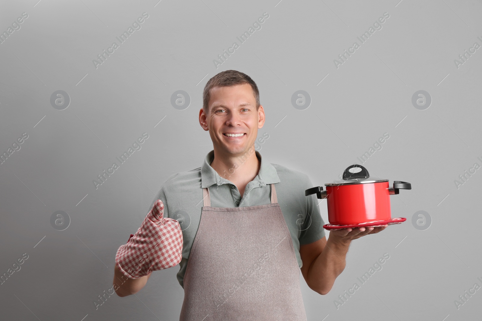 Happy man with cooking pot on light grey background Photo of Happy man with cooking pot on light grey background