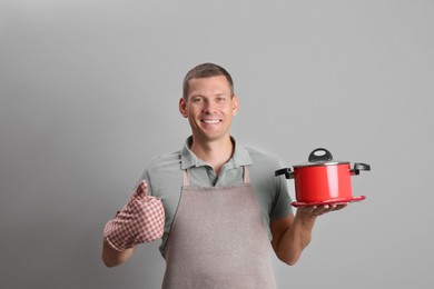 Happy man with cooking pot on light grey background Photo of Happy man with cooking pot on light grey background