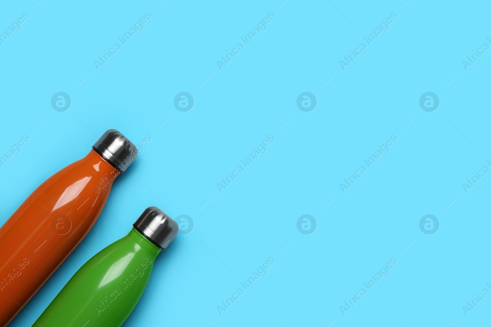 Modern thermo bottles on light blue background, flat lay. Space for text Photo of Modern thermo bottles on light blue background, flat lay. Space for text