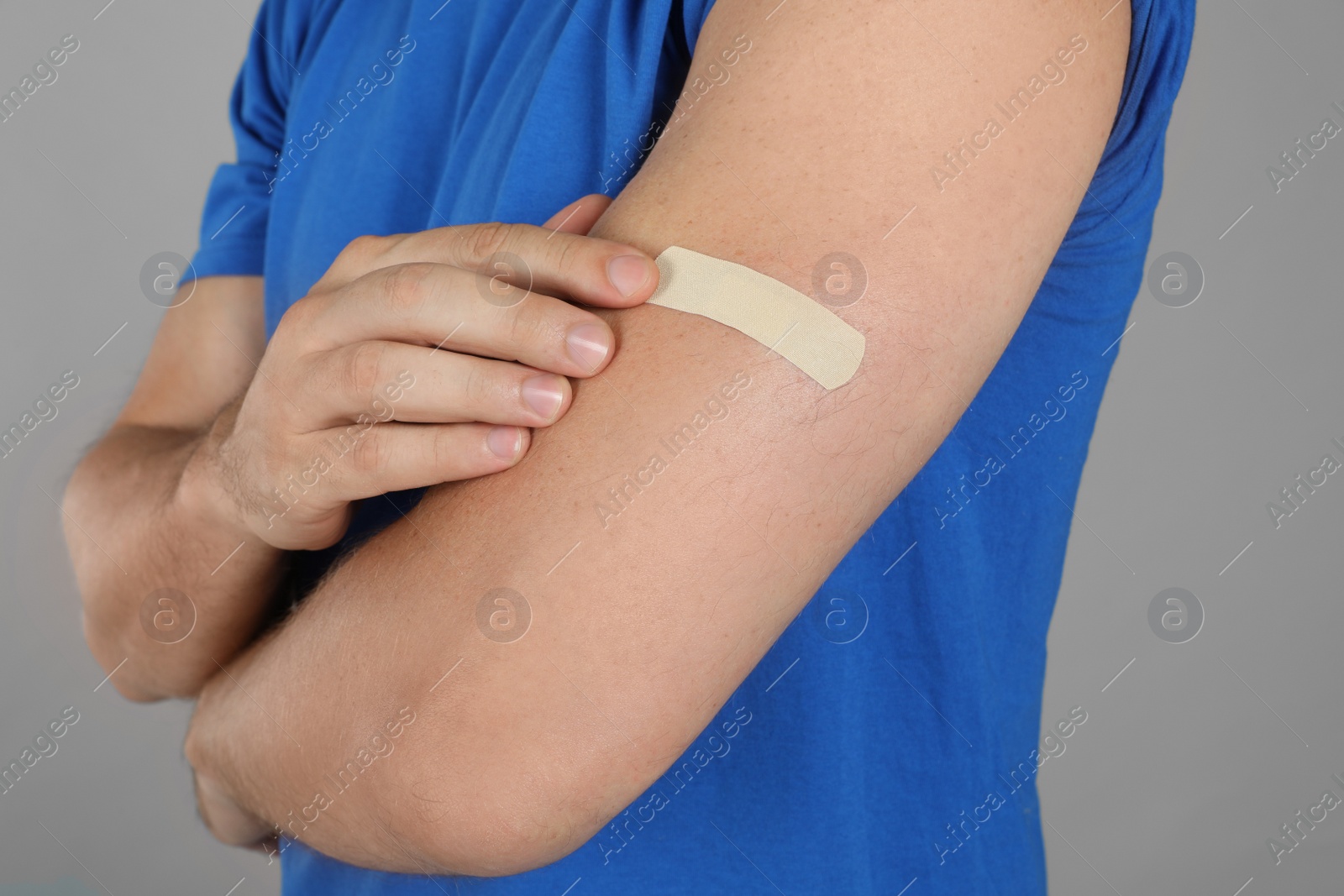Vaccinated man with medical plaster on his arm against grey background, closeup Photo of Vaccinated man with medical plaster on his arm against grey background, closeup