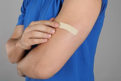 Vaccinated man with medical plaster on his arm against grey background, closeup Photo of Vaccinated man with medical plaster on his arm against grey background, closeup