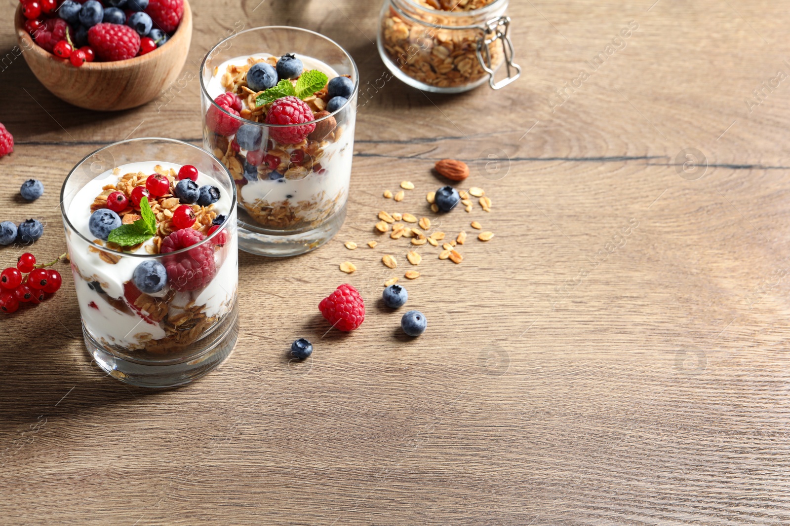Tasty dessert with yogurt, berries and granola on wooden table. Space for text Image of Tasty dessert with yogurt, berries and granola on wooden table. Space for text