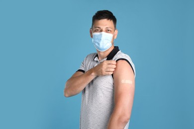 Vaccinated man with protective mask showing medical plaster on his arm against light blue background Photo of Vaccinated man with protective mask showing medical plaster on his arm against light blue background