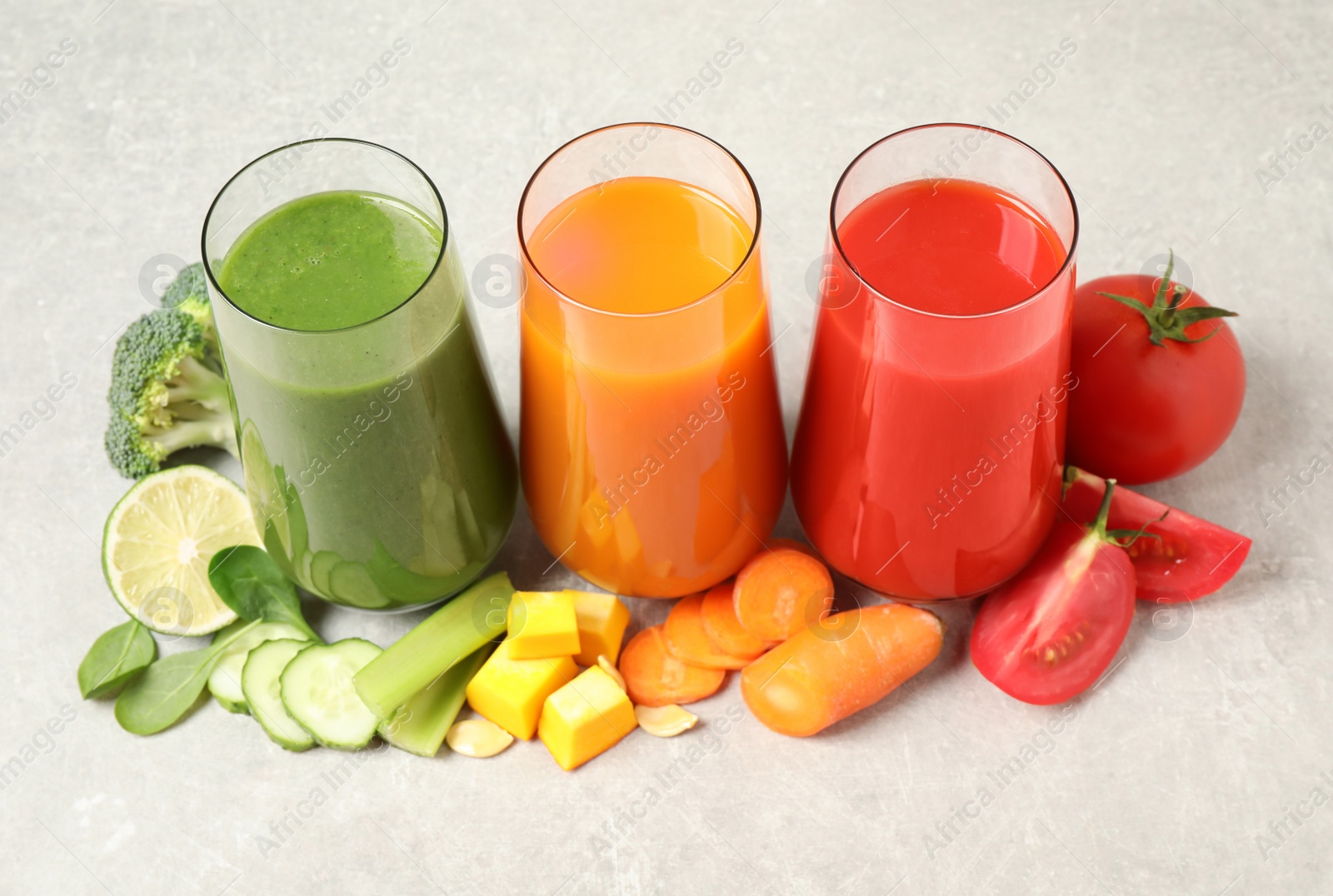 Different tasty juices and fresh ingredients on grey table Photo of Different tasty juices and fresh ingredients on grey table