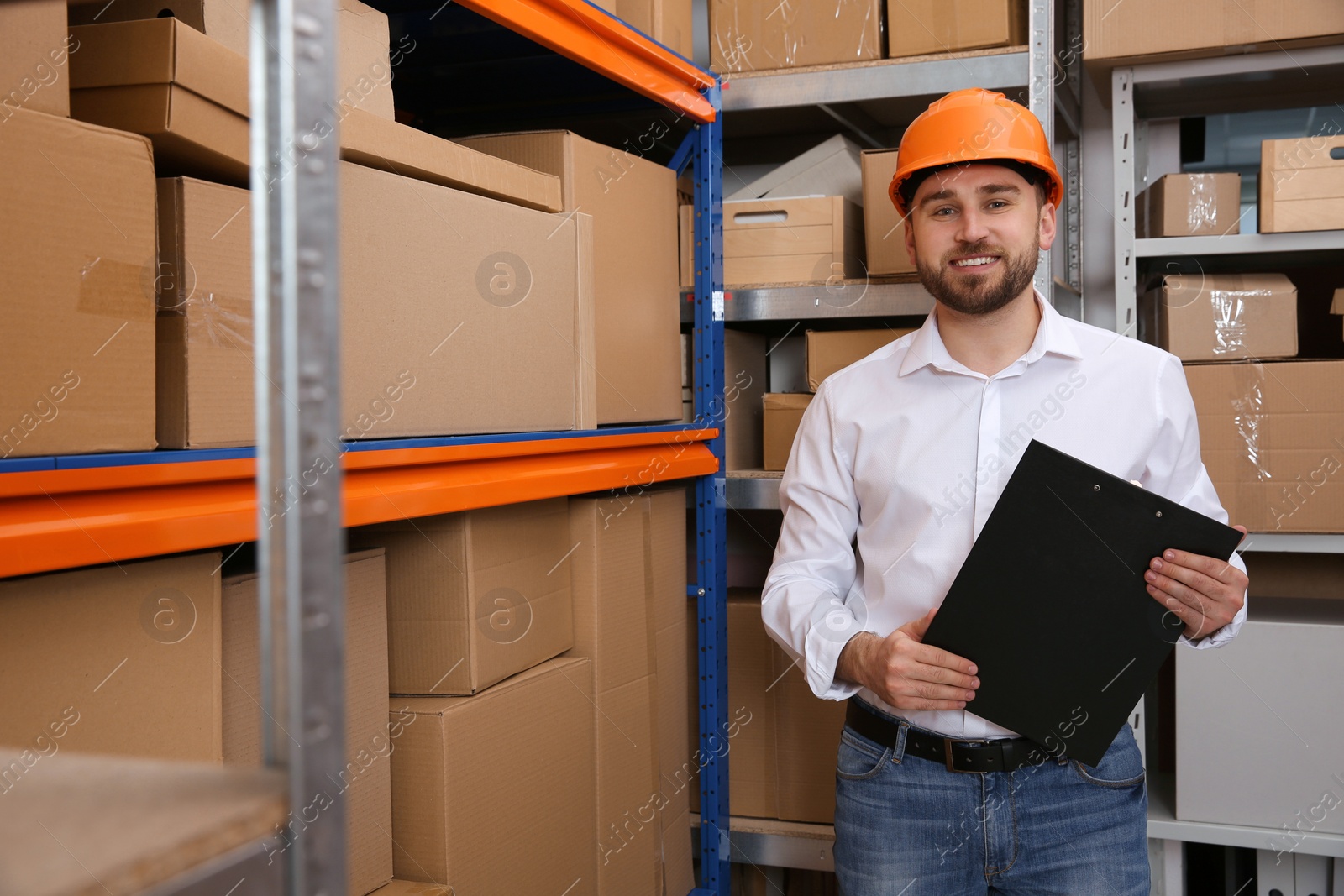Young man with clipboard near rack of cardboard boxes at warehouse Photo of Young man with clipboard near rack of cardboard boxes at warehouse