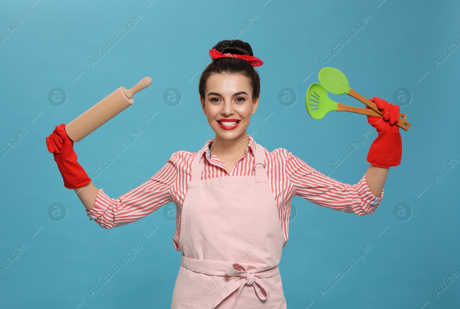 Young housewife with cooking utensils on light blue background Photo of Young housewife with cooking utensils on light blue background