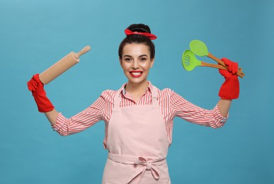Young housewife with cooking utensils on light blue background Photo of Young housewife with cooking utensils on light blue background