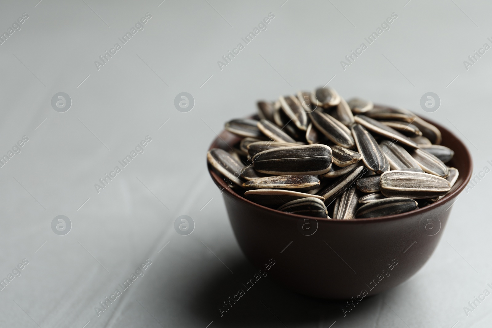 Raw sunflower seeds in bowl on grey table, closeup. Space for text Photo of Raw sunflower seeds in bowl on grey table, closeup. Space for text