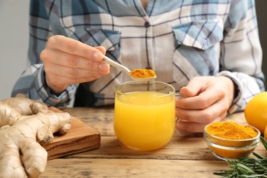 Woman adding turmeric to immunity boosting drink at wooden table with ingredients, closeup Photo of Woman adding turmeric to immunity boosting drink at wooden table with ingredients, closeup