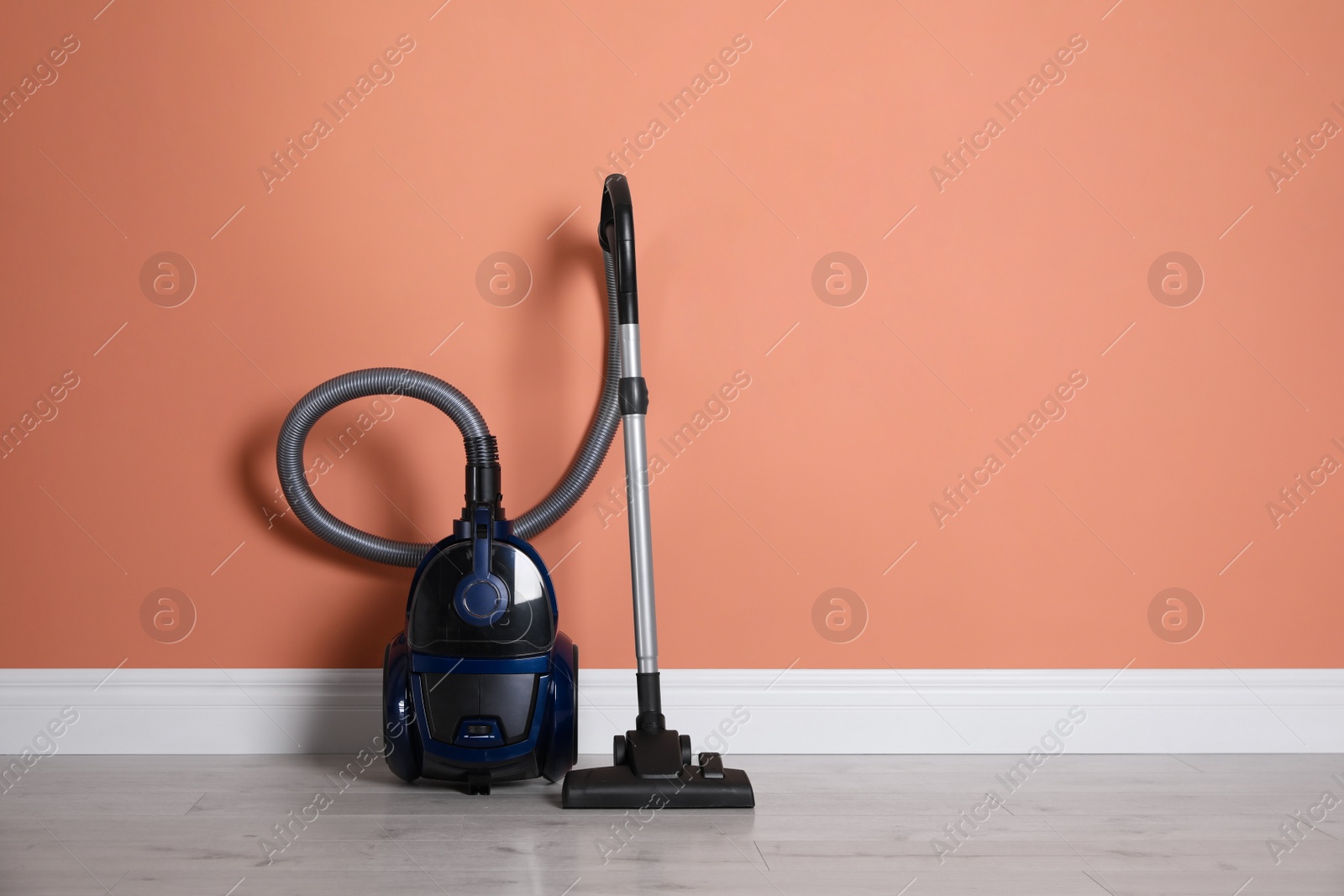 Modern vacuum cleaner on floor near orange wall indoors. Space for text Photo of Modern vacuum cleaner on floor near orange wall indoors. Space for text