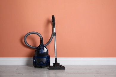 Modern vacuum cleaner on floor near orange wall indoors. Space for text Photo of Modern vacuum cleaner on floor near orange wall indoors. Space for text