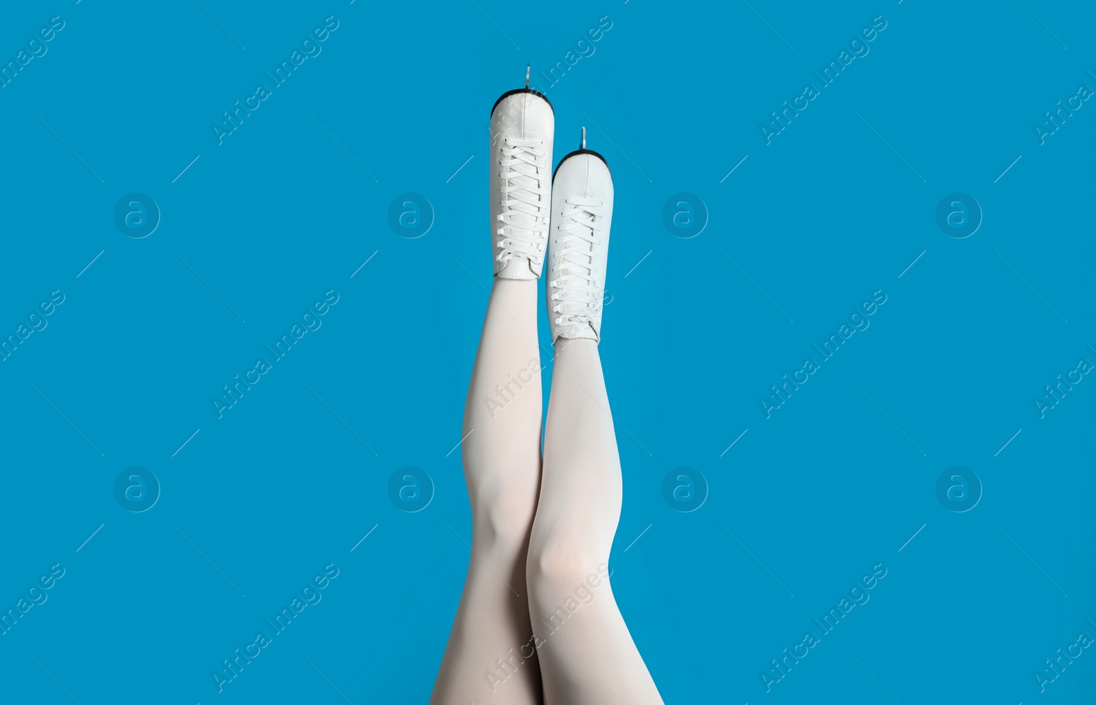 Woman in elegant white ice skates on light blue background, closeup of legs Photo of Woman in elegant white ice skates on light blue background, closeup of legs