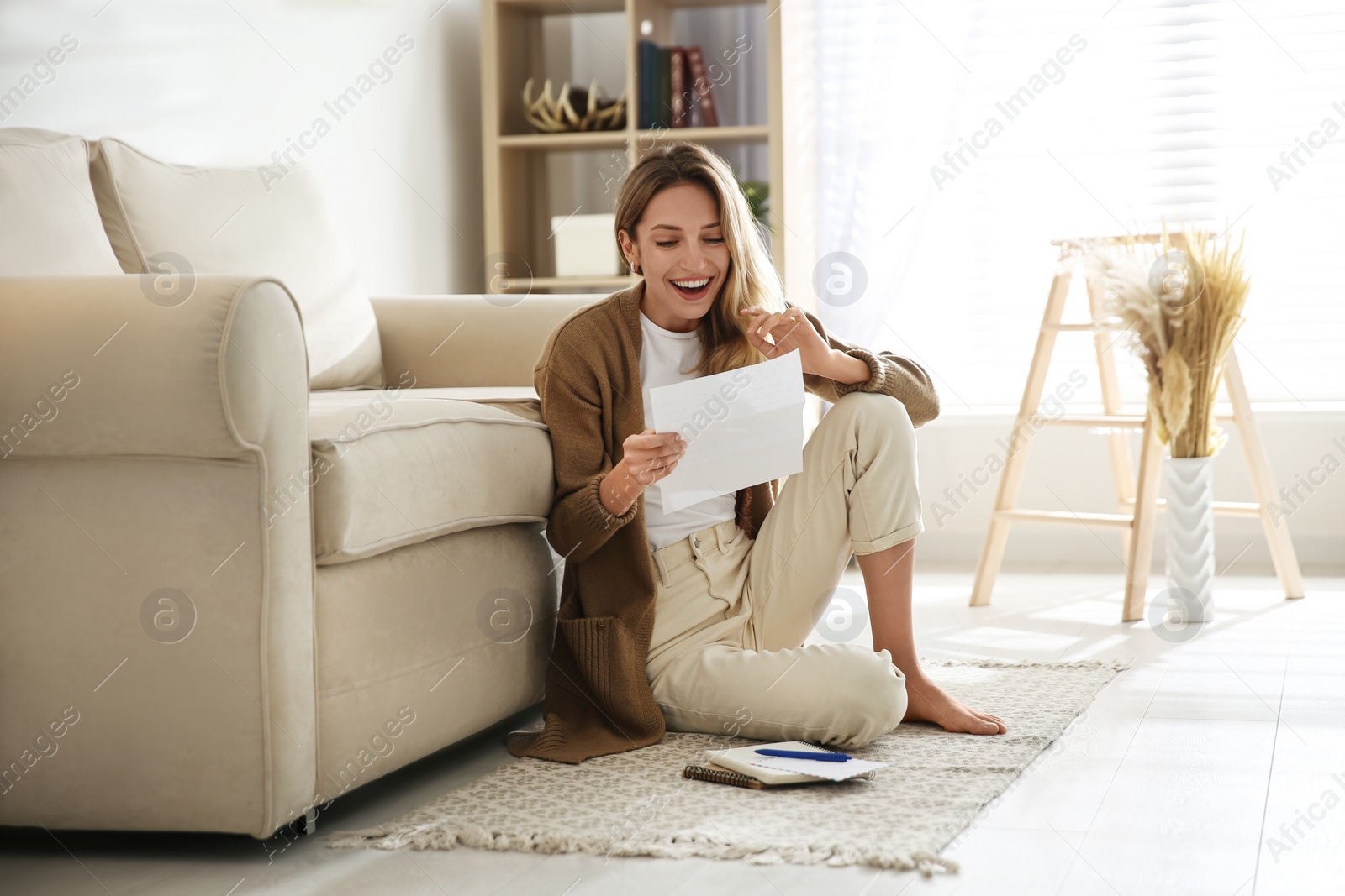 Happy woman reading letter while sitting on floor near sofa at home Photo of Happy woman reading letter while sitting on floor near sofa at home