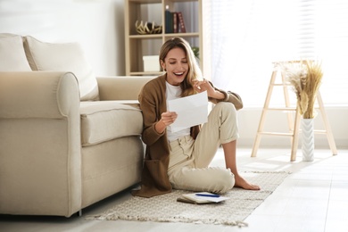 Happy woman reading letter while sitting on floor near sofa at home Photo of Happy woman reading letter while sitting on floor near sofa at home